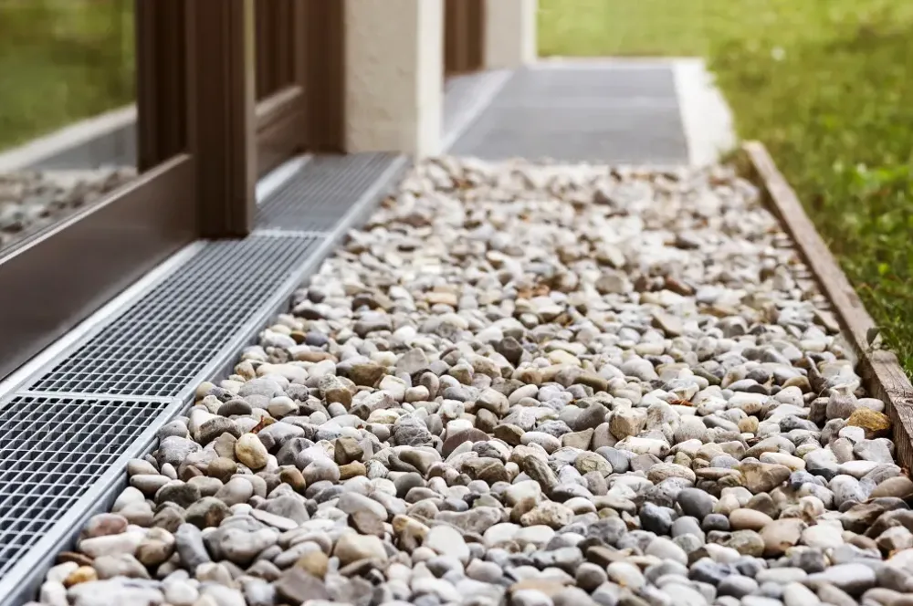 A surface channel drain beside a stone bed and exterior doors